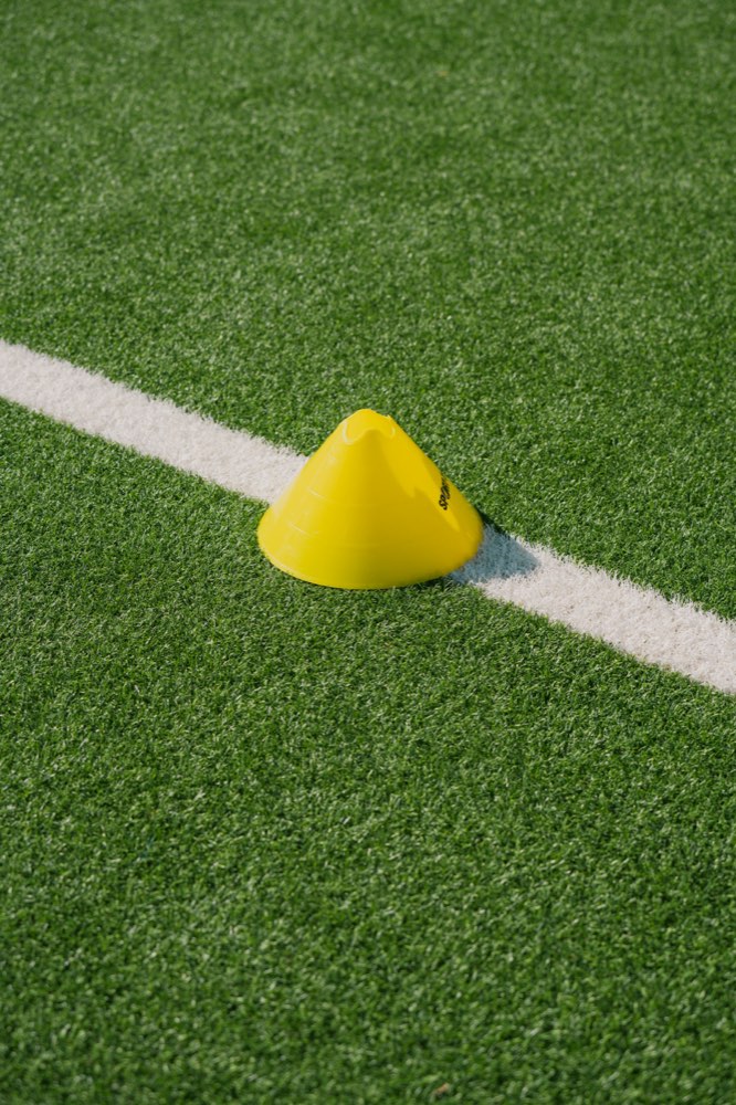 A single yellow training cone on an empty practice field